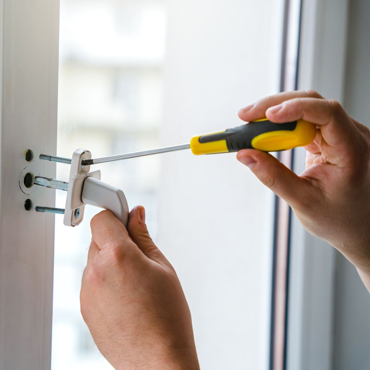 Austausch eines defekten Fenstergriffs — Hand setzt neuen Griff an und verschraubt ihn mit Schraubendreher