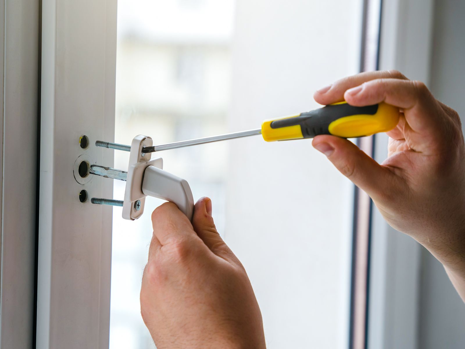 Austausch eines defekten Fenstergriffs — Hand setzt neuen Griff an und verschraubt ihn mit Schraubendreher