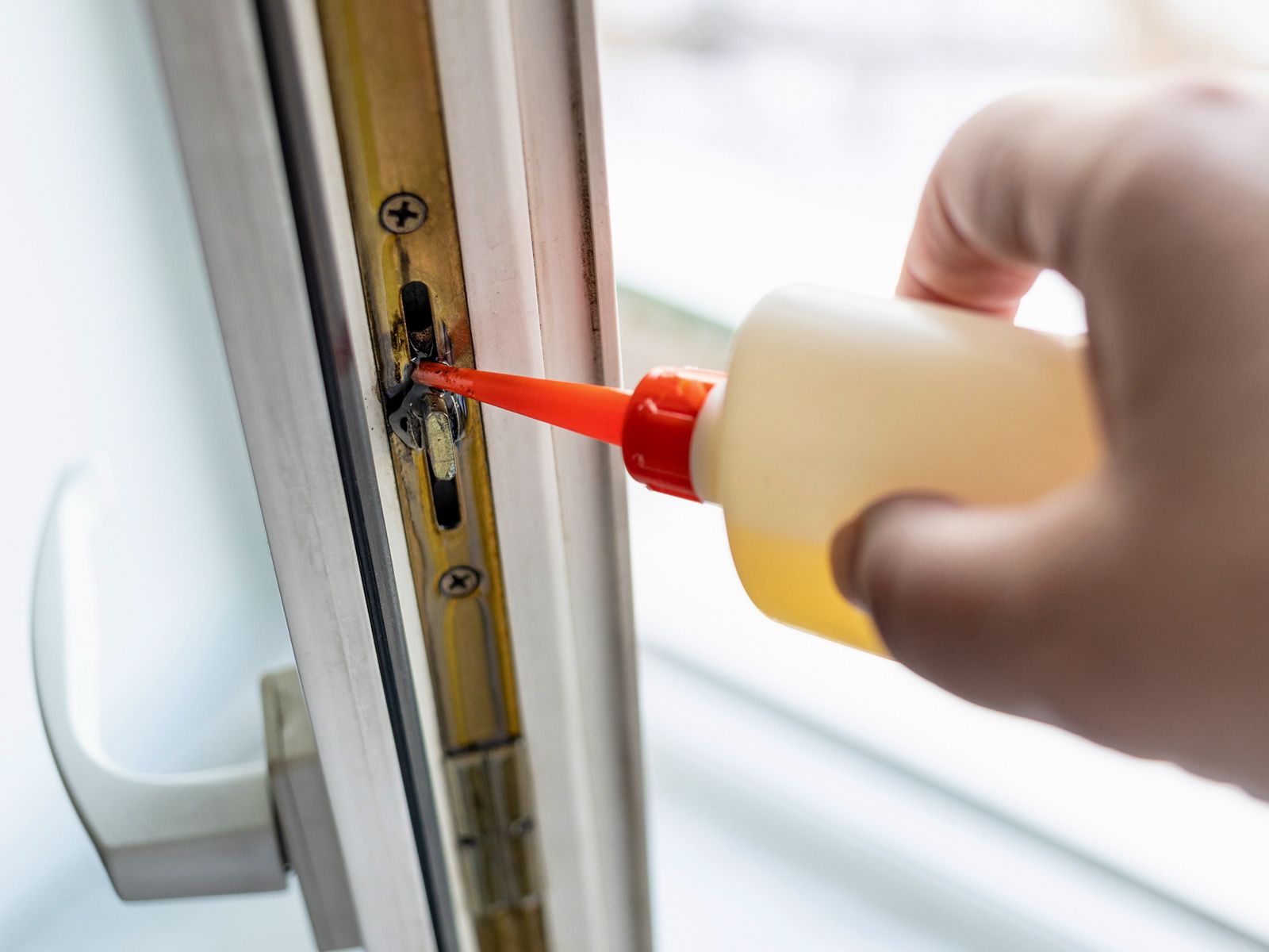 Wartung der Fenstermechanik: Beschlag am Fensterflügel wird mit Schmieröl aus einer roten Dosieröltube geschmiert