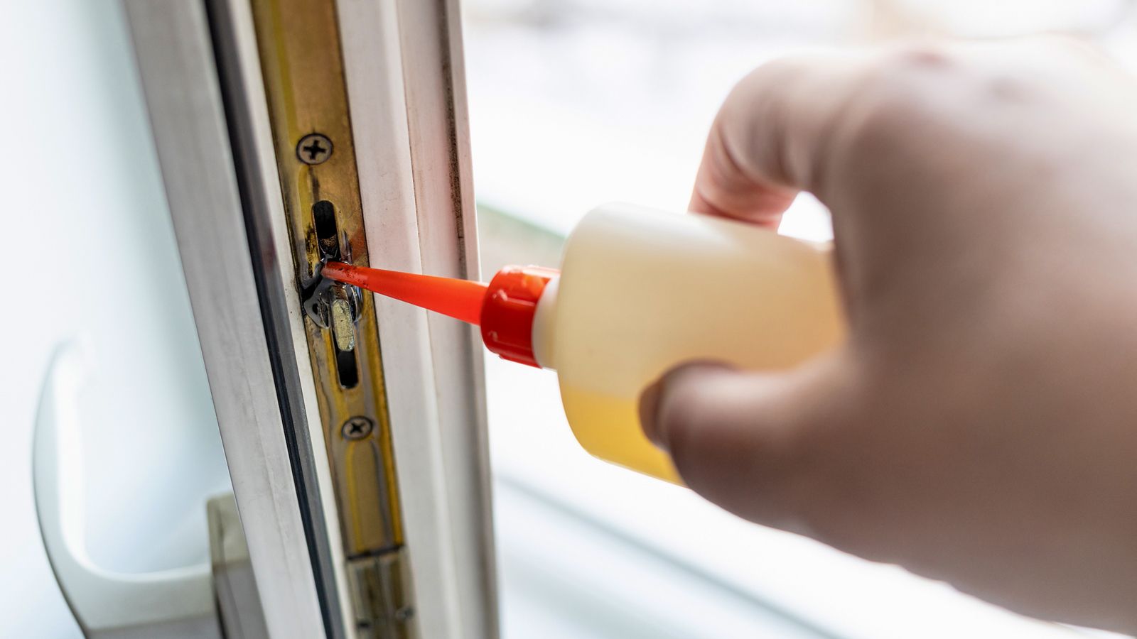 Wartung der Fenstermechanik: Beschlag am Fensterflügel wird mit Schmieröl aus einer roten Dosieröltube geschmiert