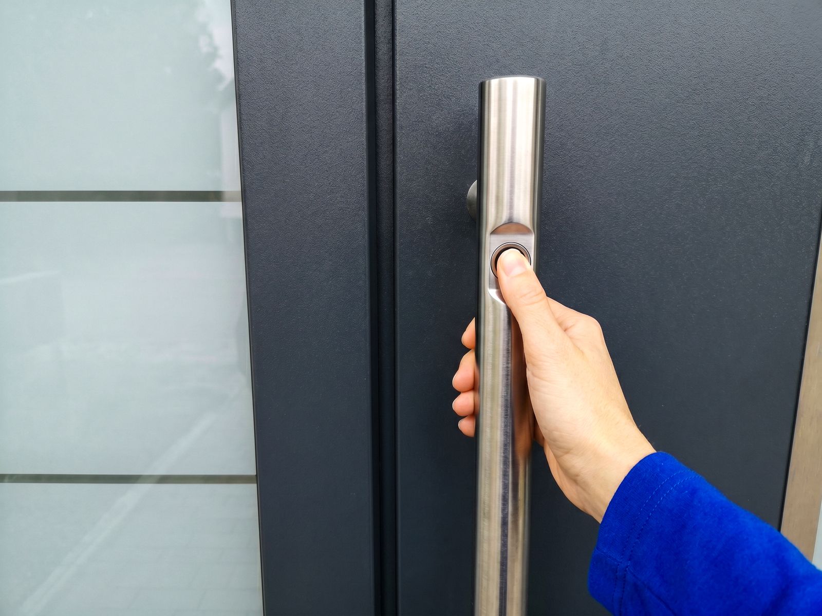 Hand legt Finger auf den Fingerabdruck-Sensor im Edelstahl-Stoßgriff einer Smart-Home-Haustür