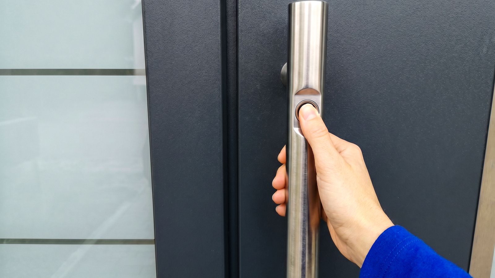 Hand legt Finger auf den Fingerabdruck-Sensor im Edelstahl-Stoßgriff einer Smart-Home-Haustür
