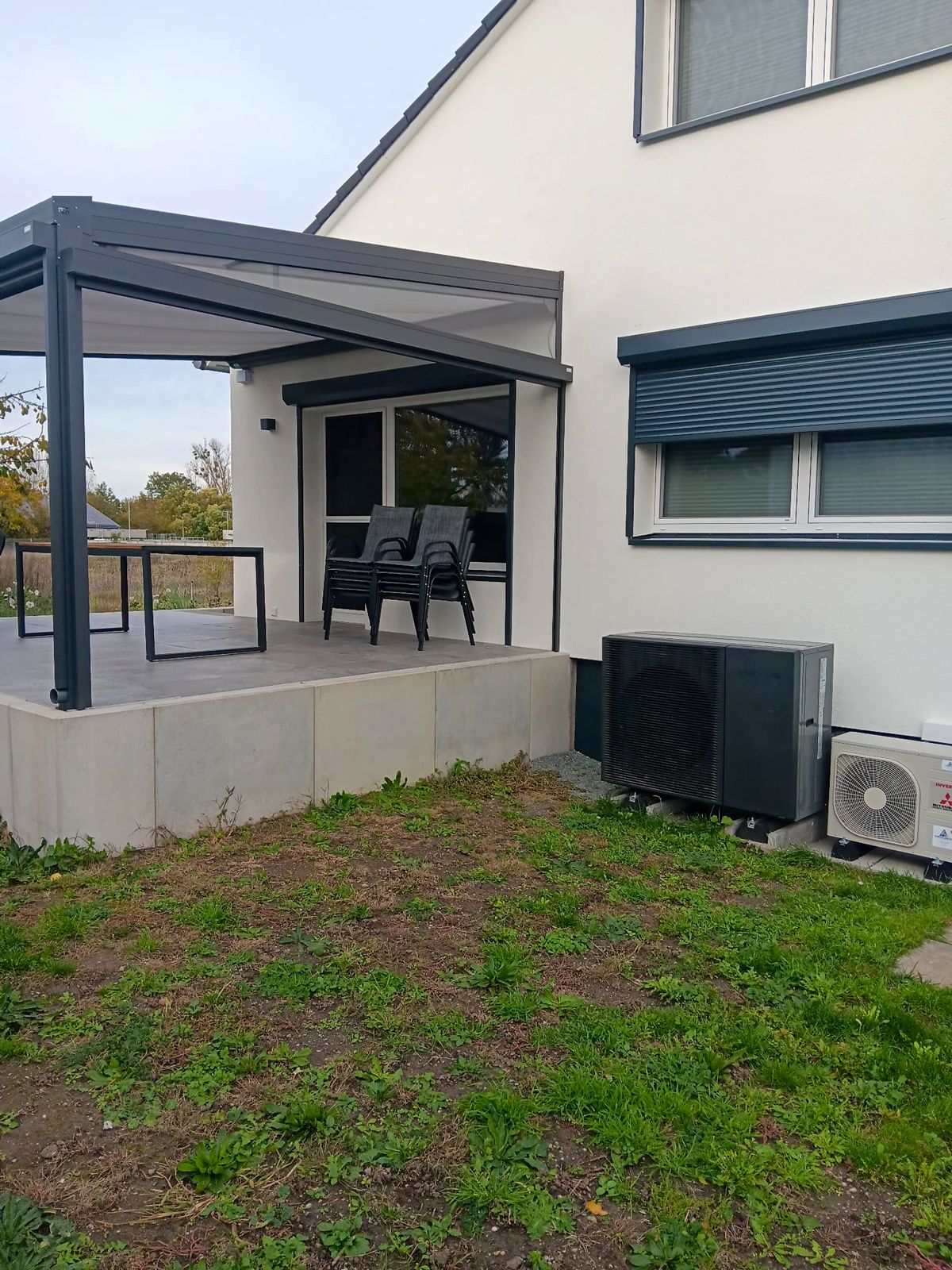 Dunkelblaue Fenster und bodentiefe Terrassentür mit Rollläden unter Überdachung