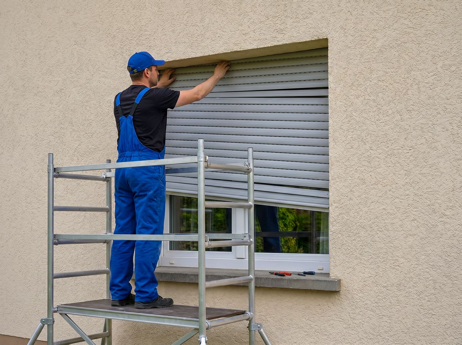 Monteur auf Arbeitsbühne repariert einen Rollladenkasten an einer Putzfassade