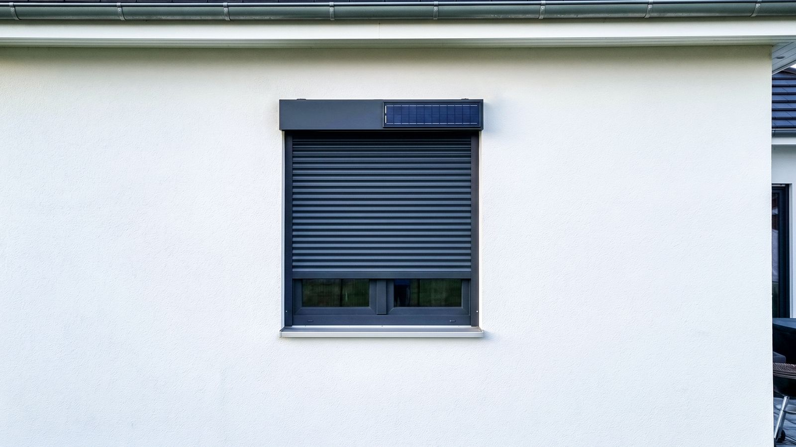 Solar-Rollladenkasten mit integriertem Solarmodul an einer weißen Putzfassade — Strom für den Antrieb ohne zusätzliche Verkabelung